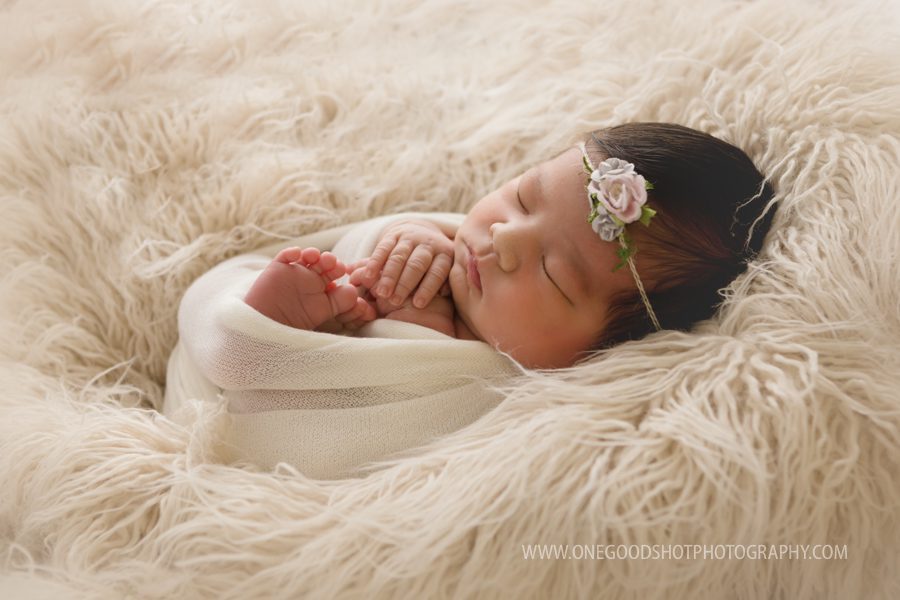 Newborn Girl wrapped in cream wrap laying on fluff