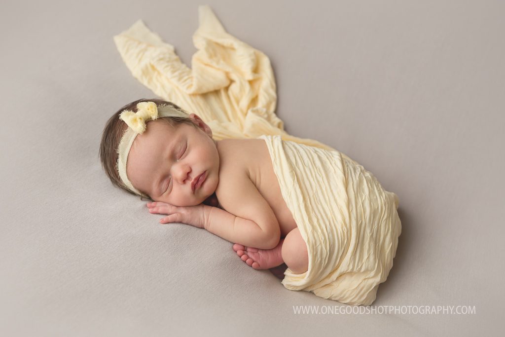 newborn girl, taco pose, gray backdrop, yellow wrap and bow