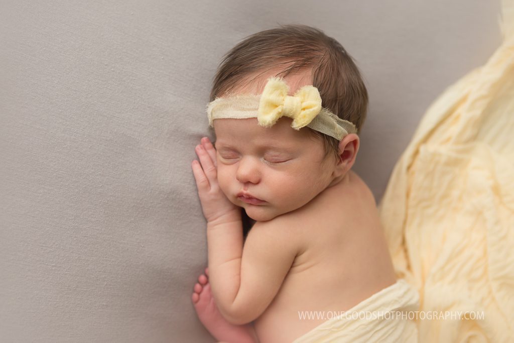 newborn girl, close up taco pose, gray backdrop, yellow wrap, yellow bow