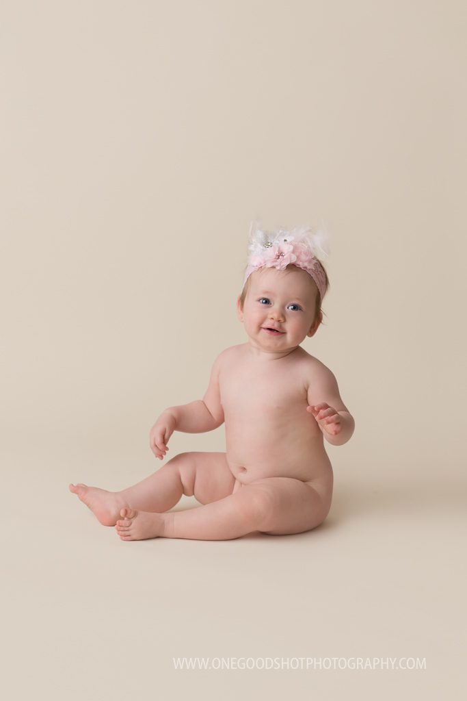 one year old girl sitting naked wearing pink bow