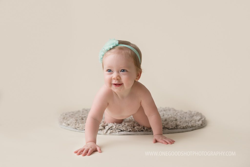 one year old girl crawling towards camera on gray rug wearing teal bow