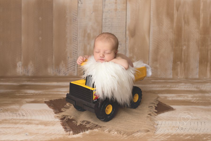 newborn boy, propped in tonka truck, white fur, wood backdrop