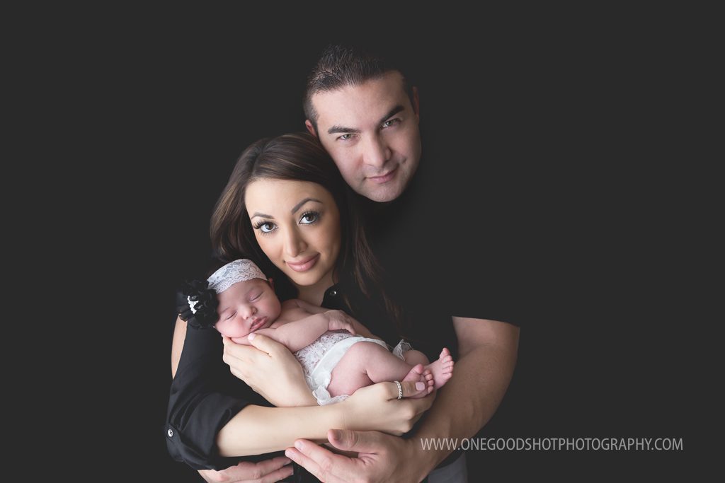 new parents, mom and dad holding newborn girl, dressed in black, black background