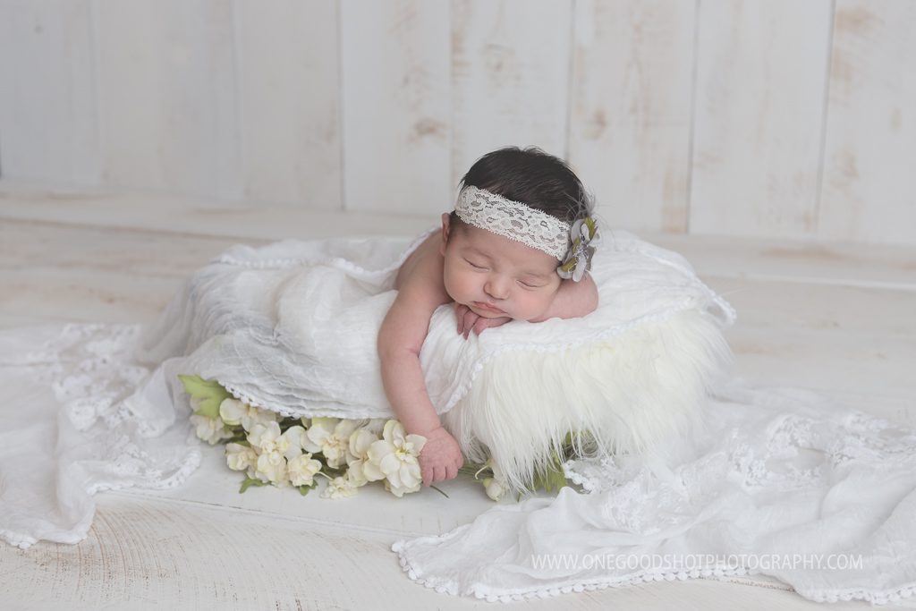 newborn girl, posed in bowl with white lace, white fluff, and flowers