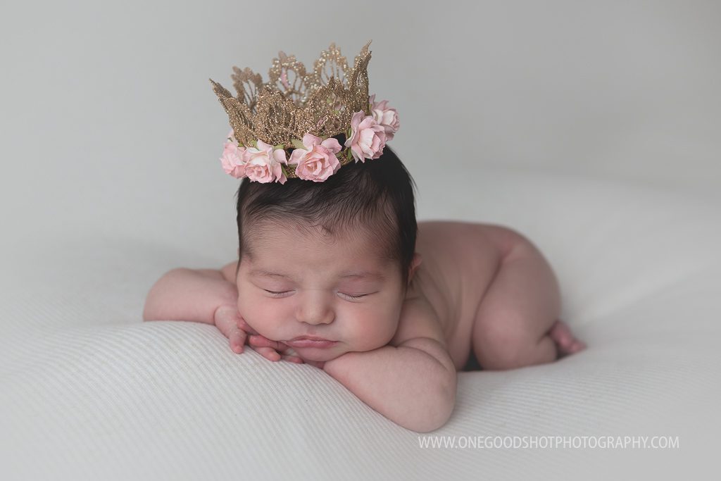 newborn girl wearing princess gown, head on hands