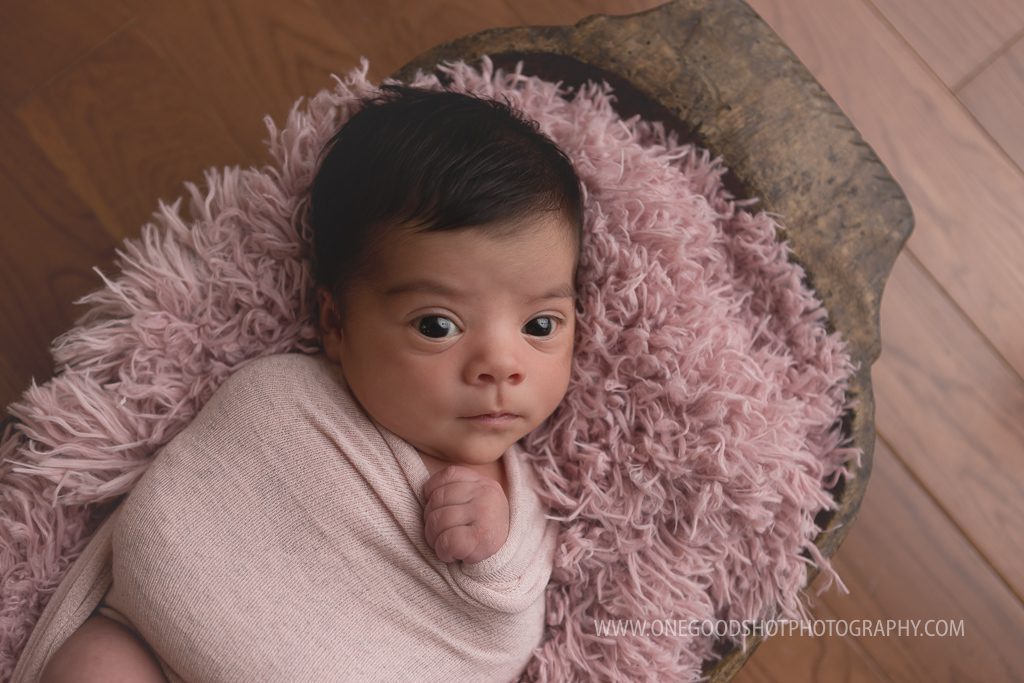 Newborn girl, awake, beautiful brown eyes, wrapped in pink, in a bowl, dainty tieback
