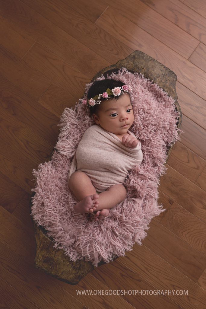 Newborn girl, awake, beautiful brown eyes, wrapped in pink, in a bowl, dainty floral halo
