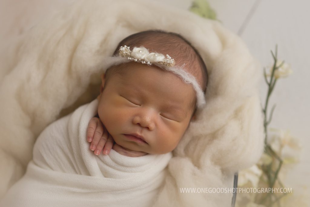 newborn girl wrapped in cream wearing dainty tieback and lying in a bowl of fluff fresno photographer