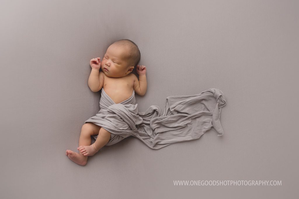 newborn girl baby led posing wrapped in gray on a gray backdrop fresno photographer