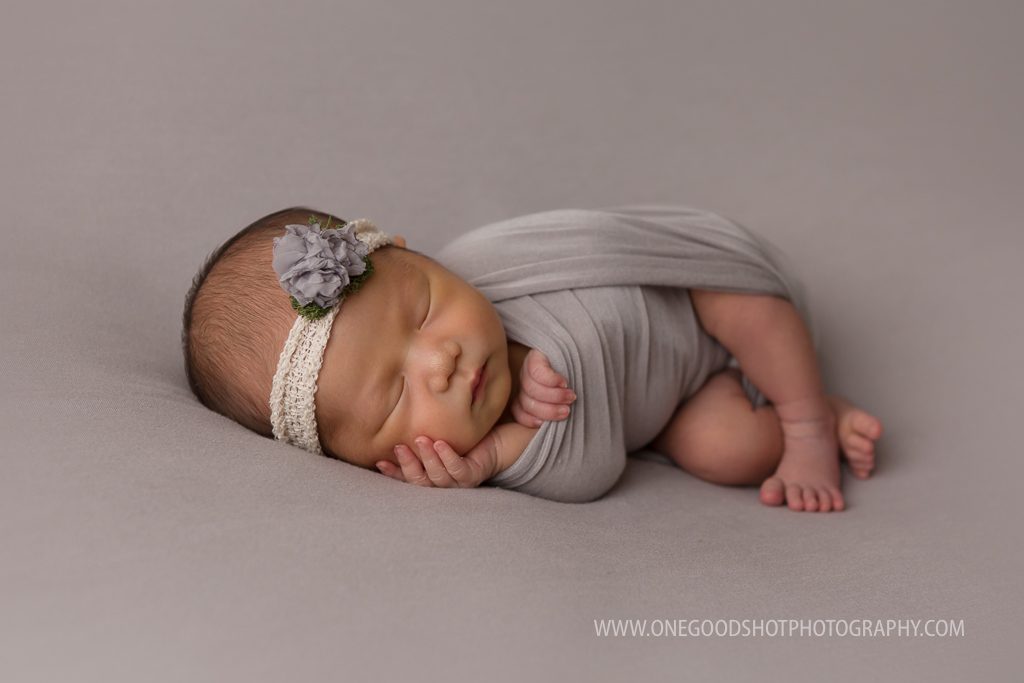 newborn girl side lying with hands up by face wrapped in gray on a gray backdrop fresno photographer