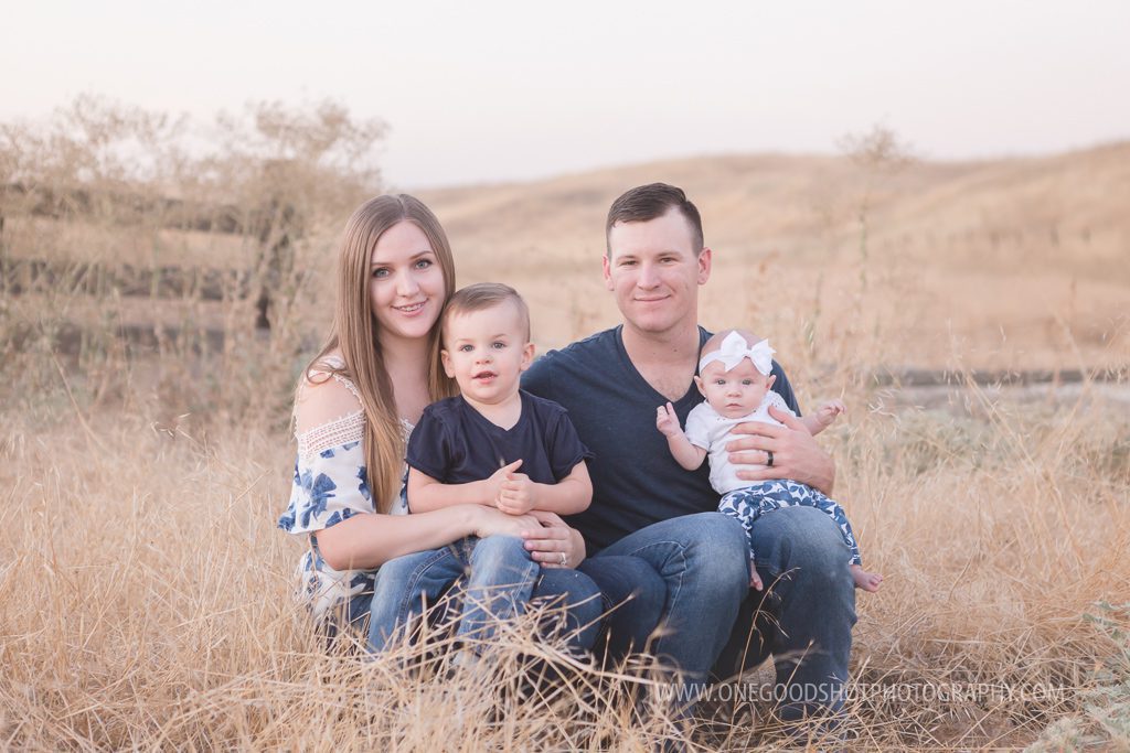 family sitting in a wheat grass field, son on mom's lap, baby girl on dad's lap, rustic image, fresno family photographer