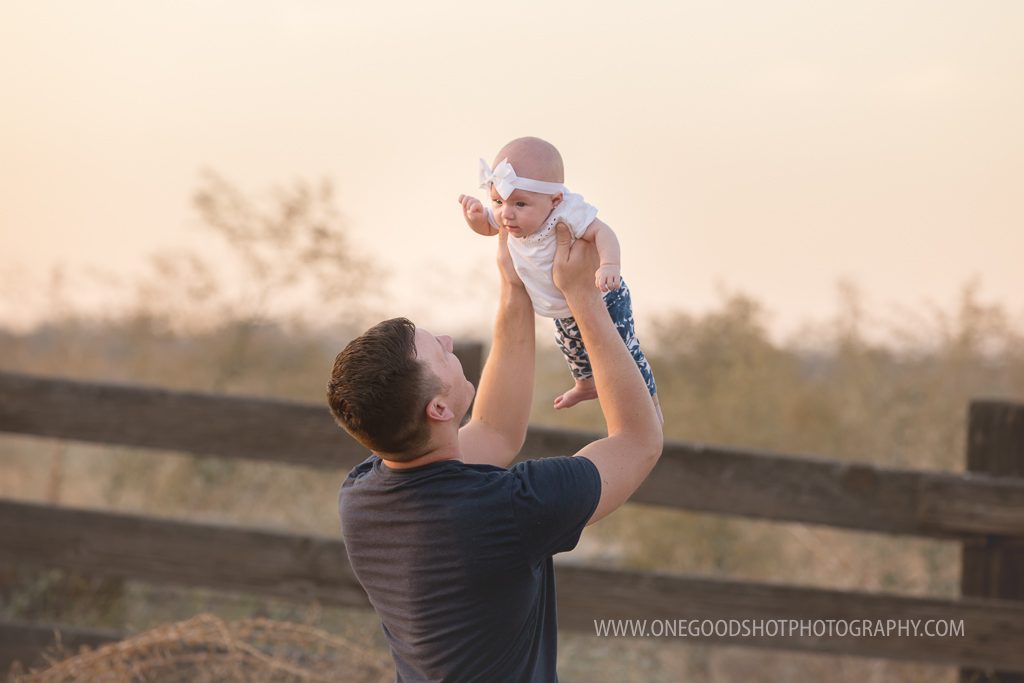 Dad holding baby girl up above him in a wheat grass field, backlit, fresno baby photographer