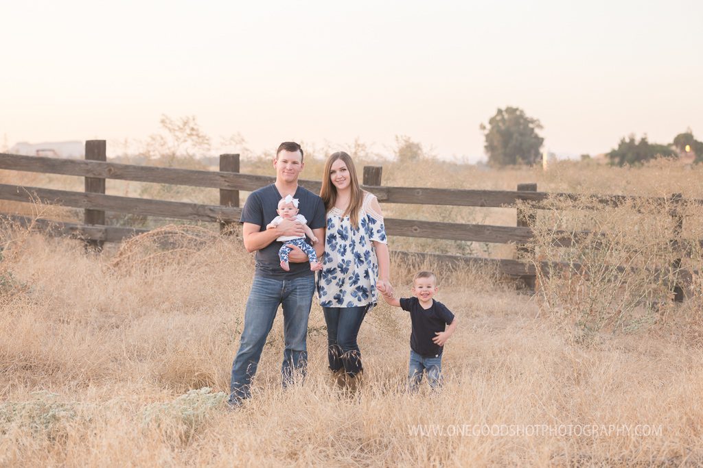 Family standing in a wheat grass field, dad holding baby girl, mom holding young sons hand, fresno family photographer