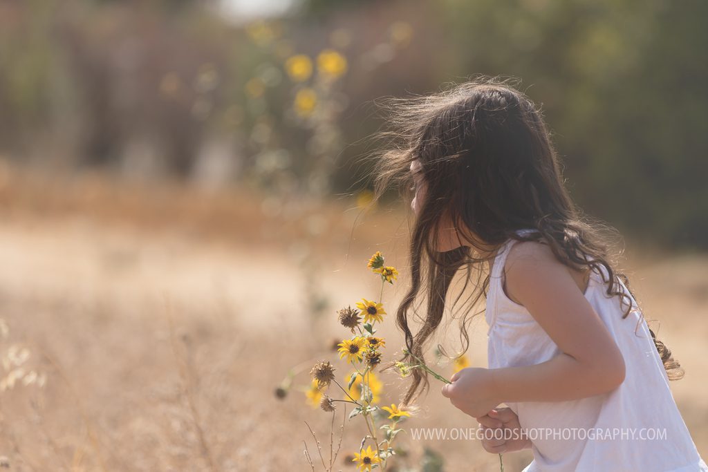 girl in field smelling yellow wildflowers, wearing a white dress