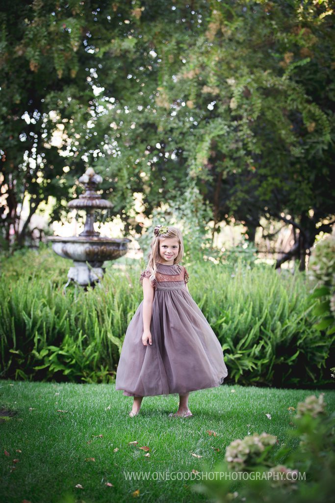 little girl twirling in a vintage brown dress in a garden with a fountain in the background