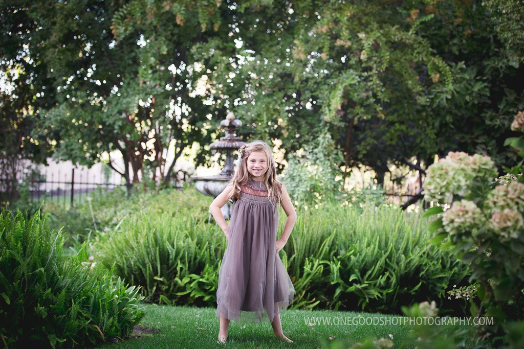 little girl twirling in a vintage brown dress in a garden with a fountain in the background