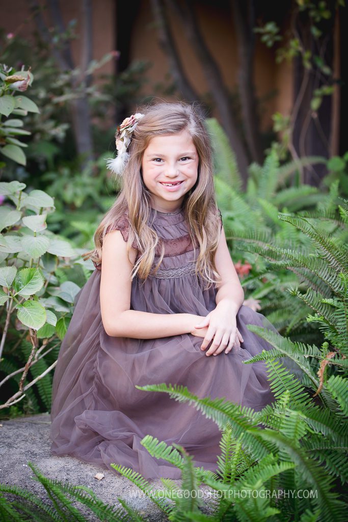 little girl wearing vintage brown dress, sitting in green garden