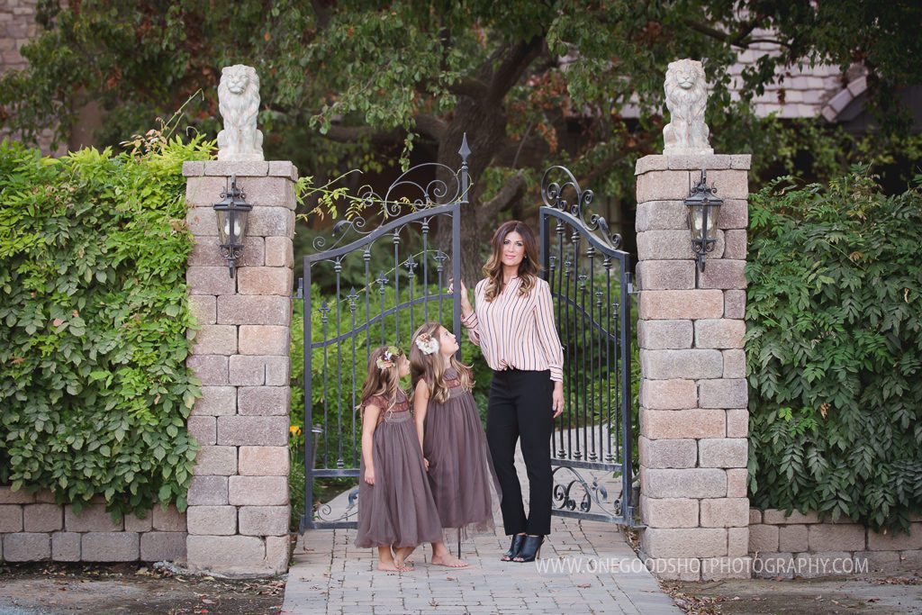 Daughters wearing vintage brown dress looking up at mom standing in front of a wrought iron gate