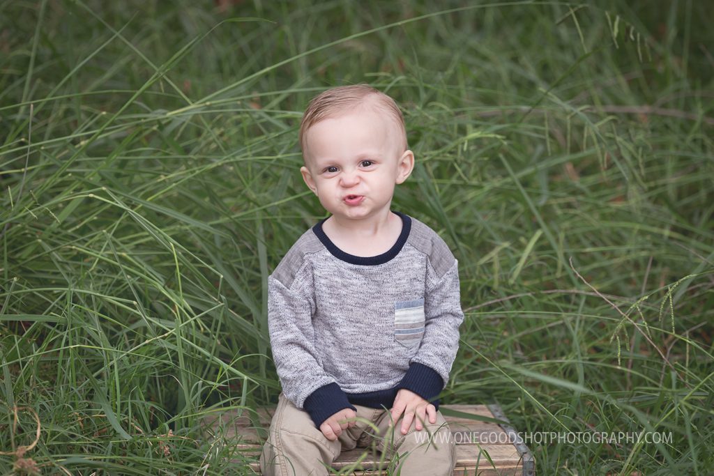 baby boy in tall grass sitting on a box making a kissy face