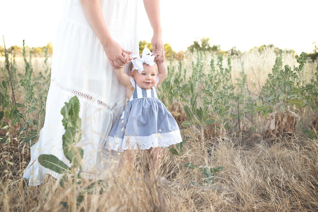 Fresno baby photographer, mom and baby girl holding hands in a field