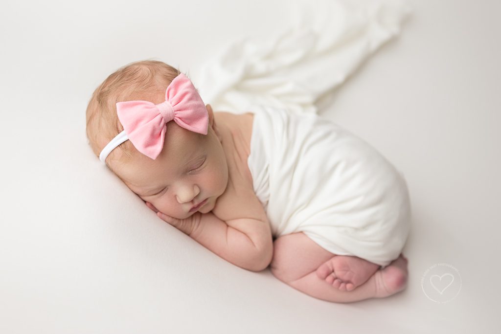 Newborn baby girl, tushy up, covered with white blanket, pink bow headband