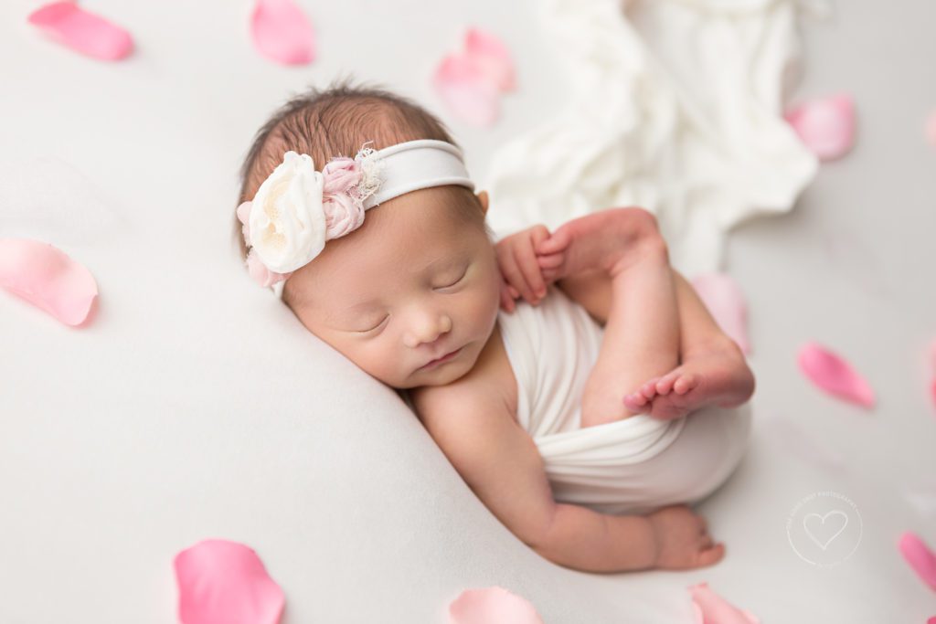 Fresno newborn photographer, baby girl in luck Finn pose, wrapped in white , with pink flower petals