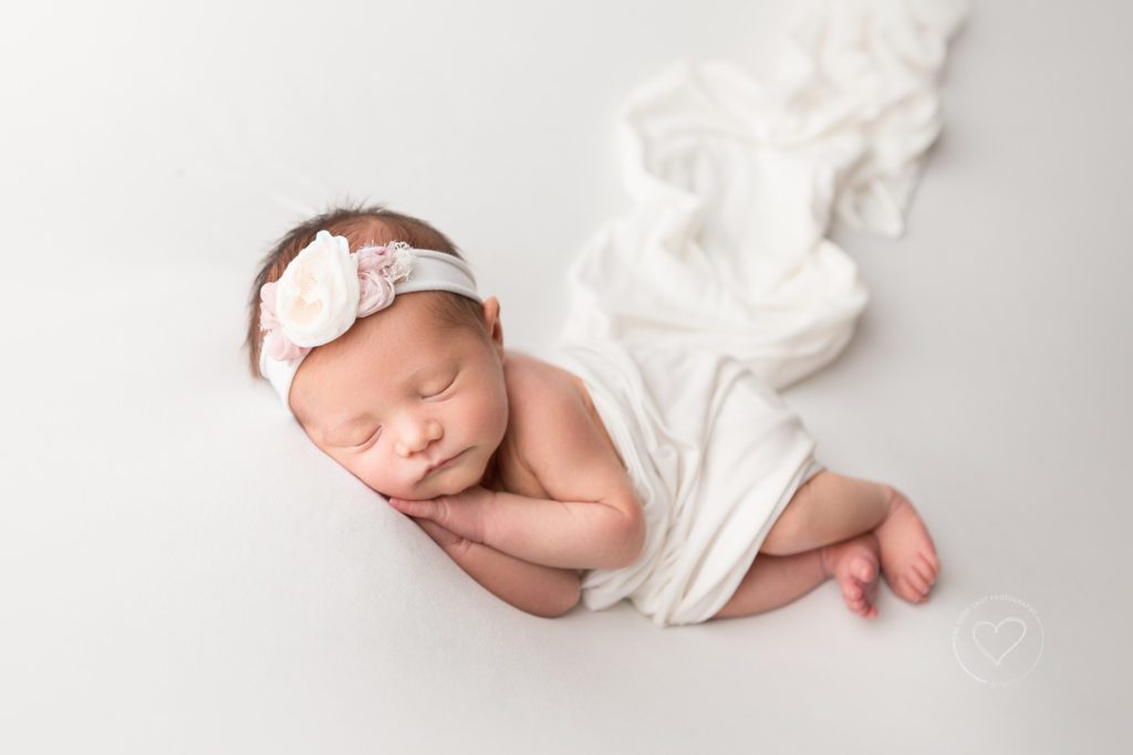 Fresno newborn photographer, baby girl side lying with hands under cheek, covered with white wrap