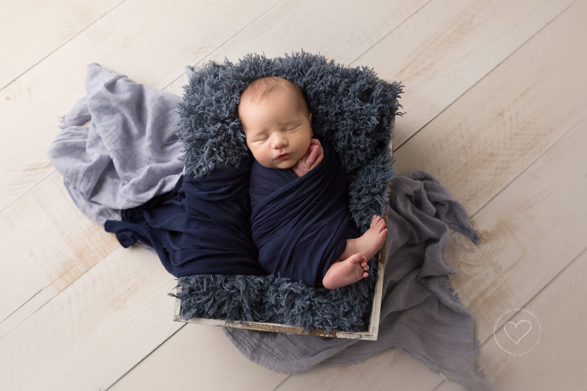 Newborn boy wrapped in navy, laying in a box, white wood background, Fresno, Clovis, ca