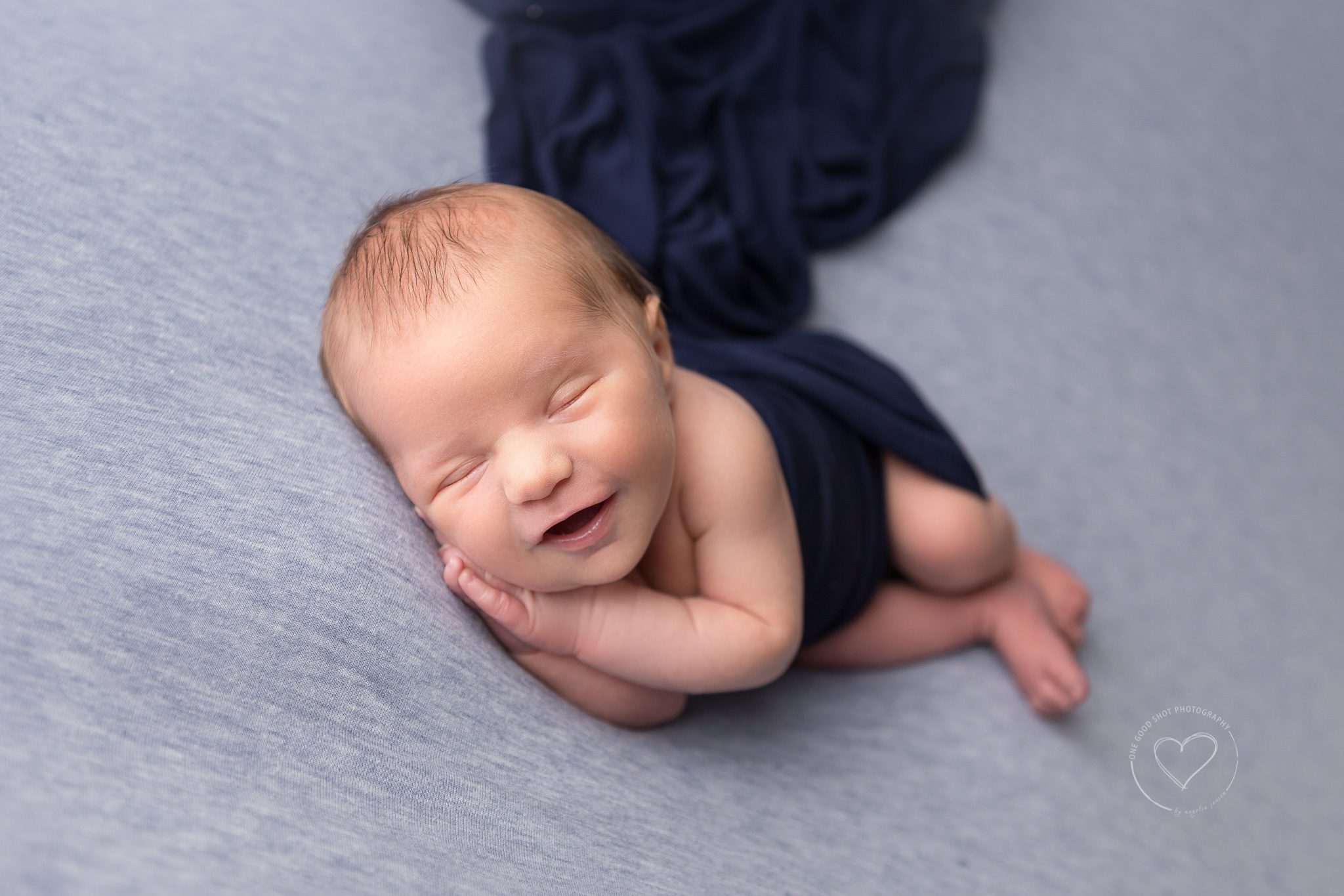 newborn boy, side lying, smiling, blue backdrop, navy wrap