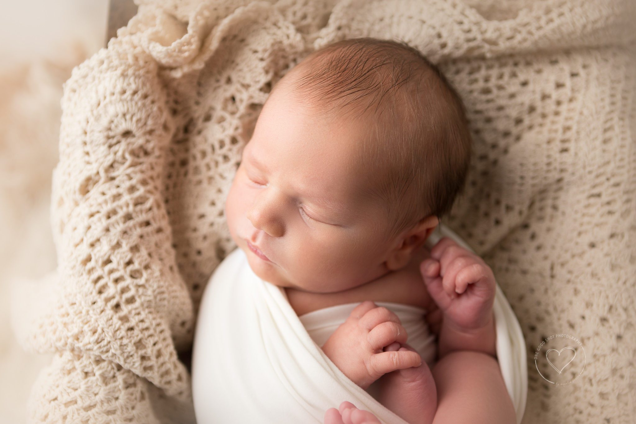 Newborn boy, wrapped in white, lying on vintage overlay, close up