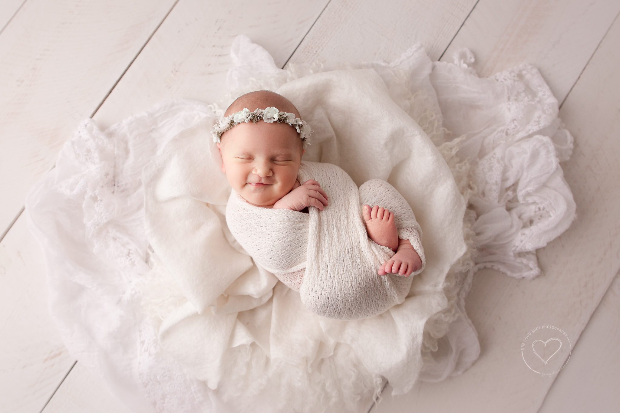 Fresno newborn photography, baby girl wrapped in white, white layers, wood backdrop, white floral halo, baby smiling