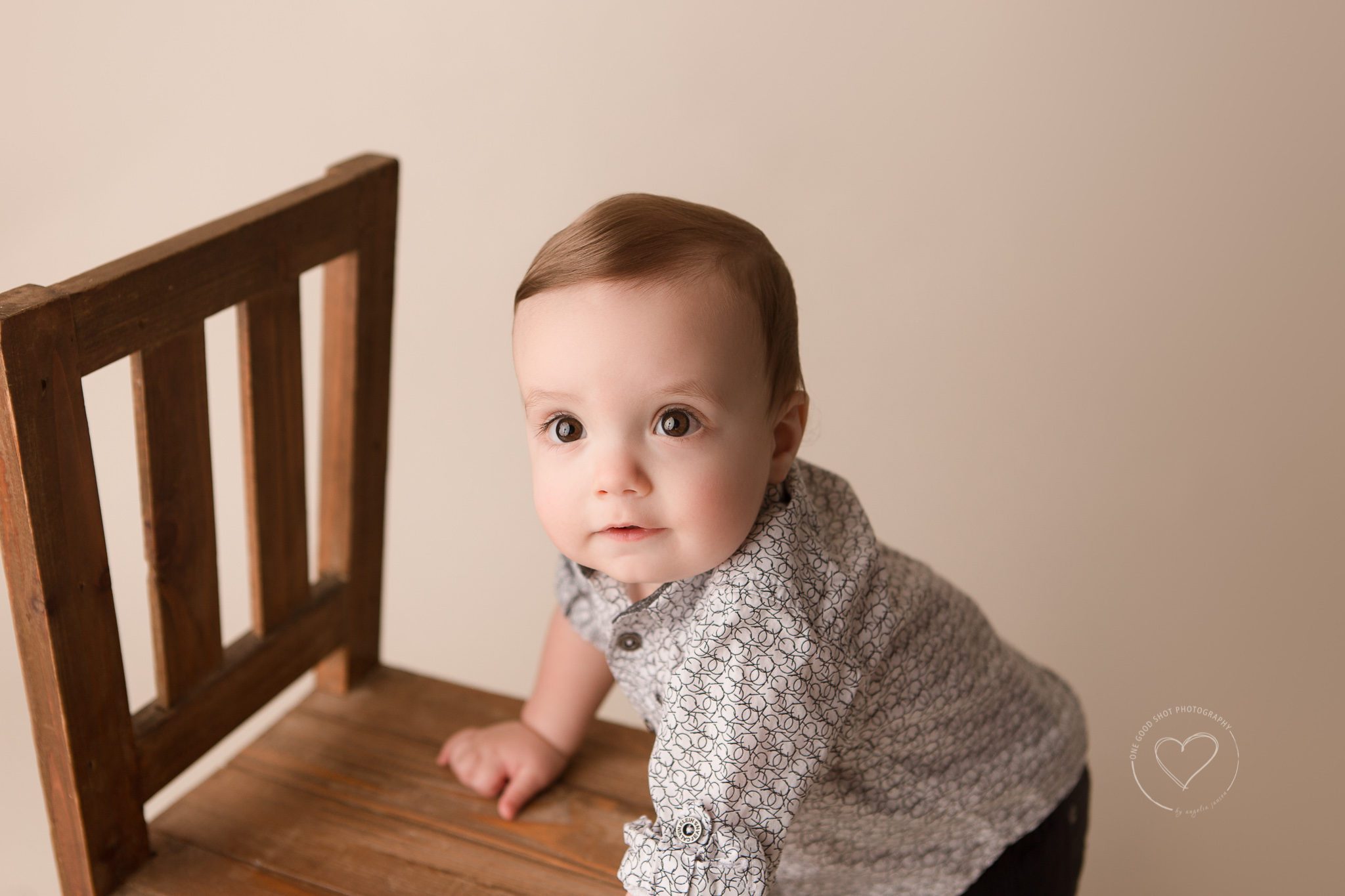 Fresno baby photographer, lboy leaning on brown chair smiling, 9 month old