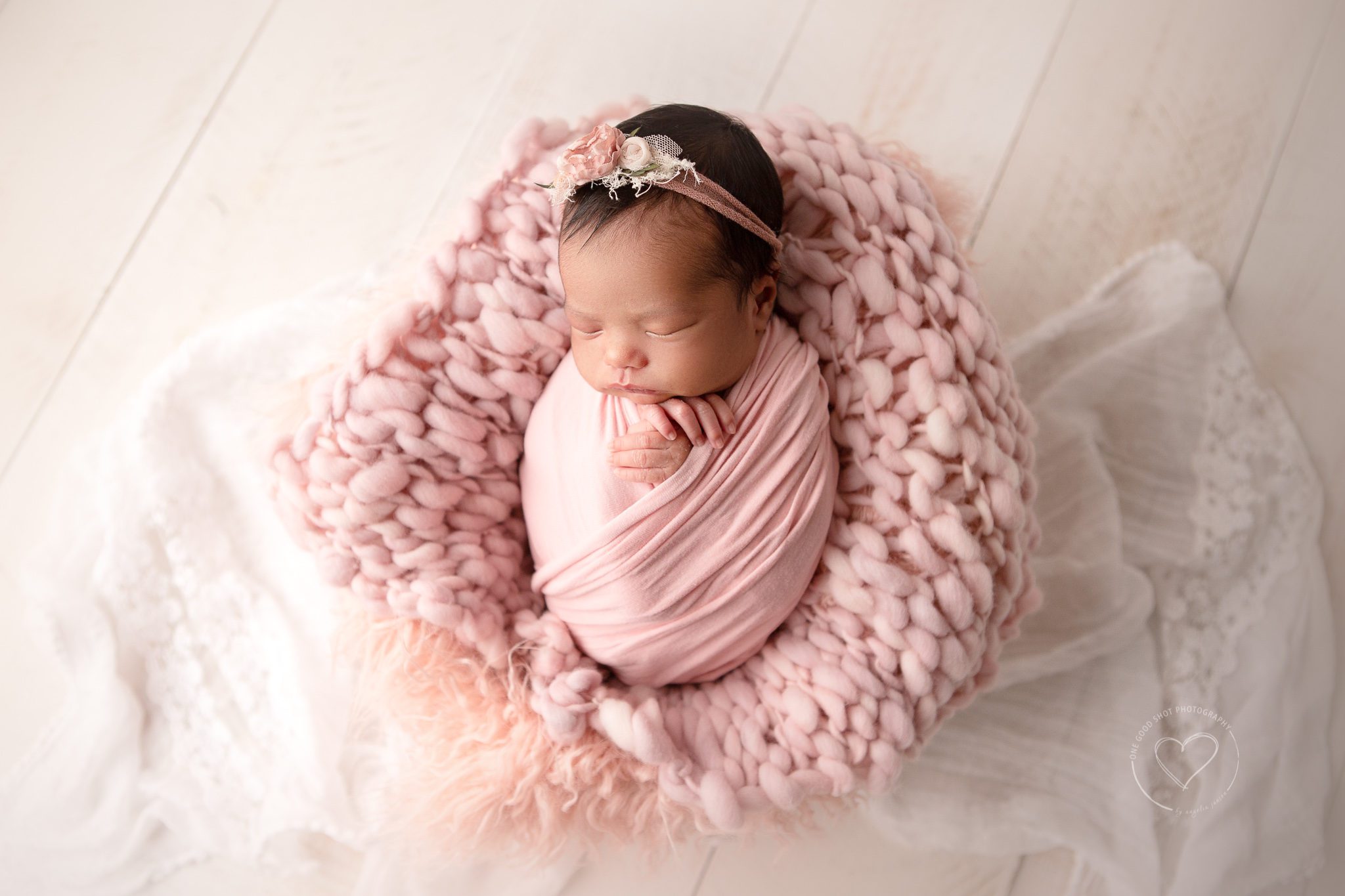 Newborn girl wrapped in pink, on pink wool layer, wearing a floral headband