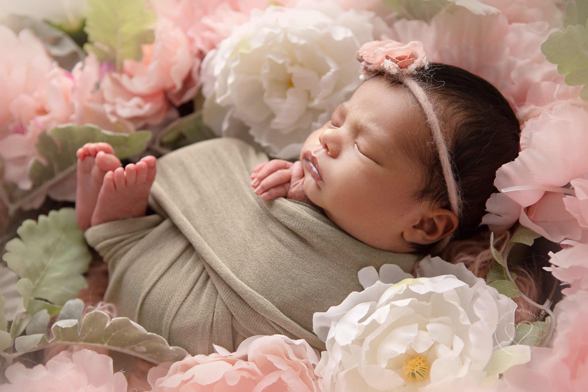 Newborn girl, wrapped in light green, fingers and toes showing, lying in floral wreath