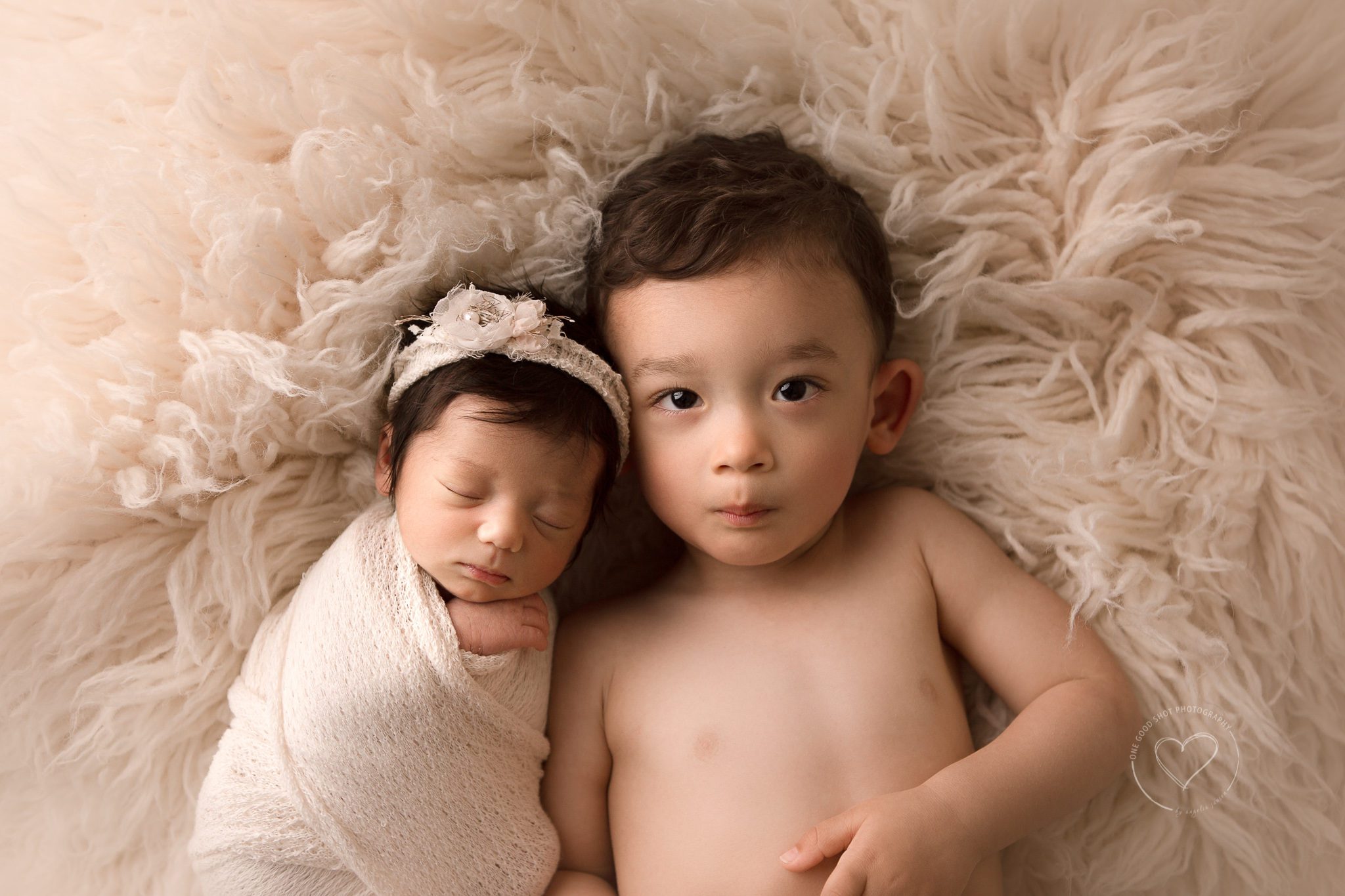 Sibling photo, Big brother lying next to newborn sister, baby girl wrapped in white wearing floral headband, fresno newborn photographer 