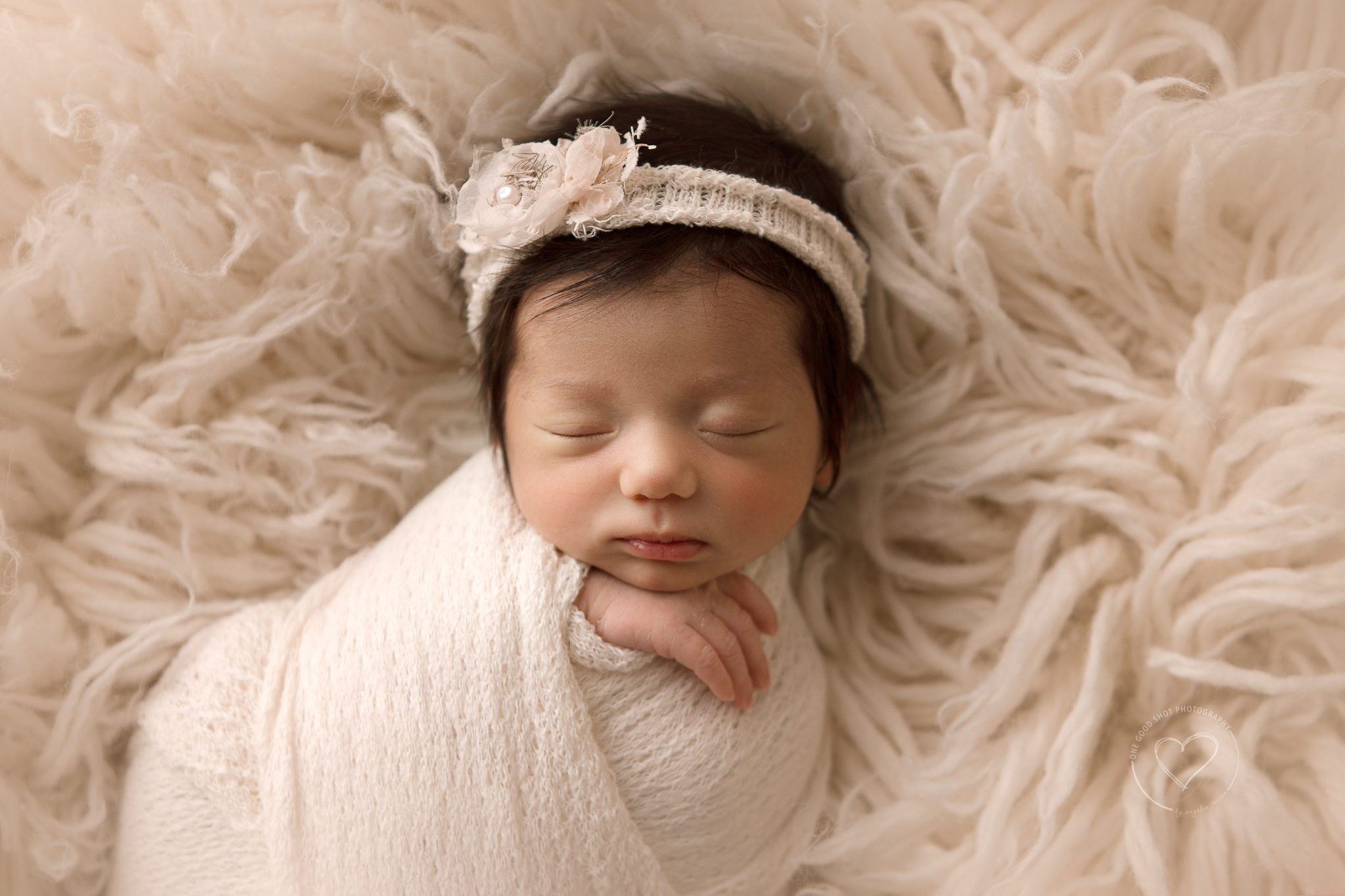 Newborn girl wrapped in cream lying on flokati rug.  Hands showing, wearing floral headband, fresno newborn photographer 