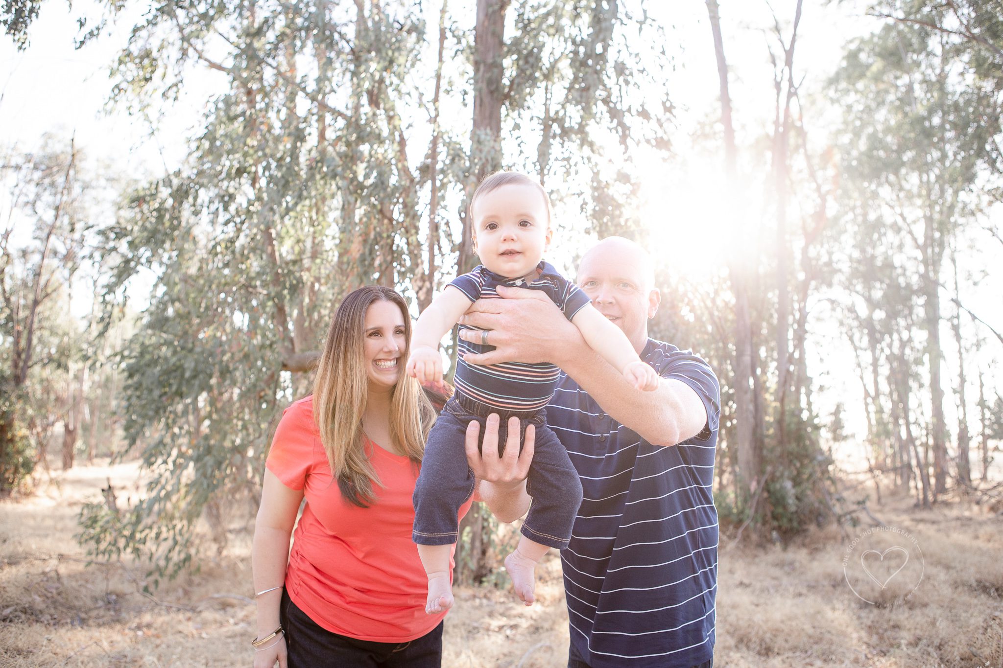 Mom and dad swinging baby towards camera, Fresno family photographer, backlit in a field