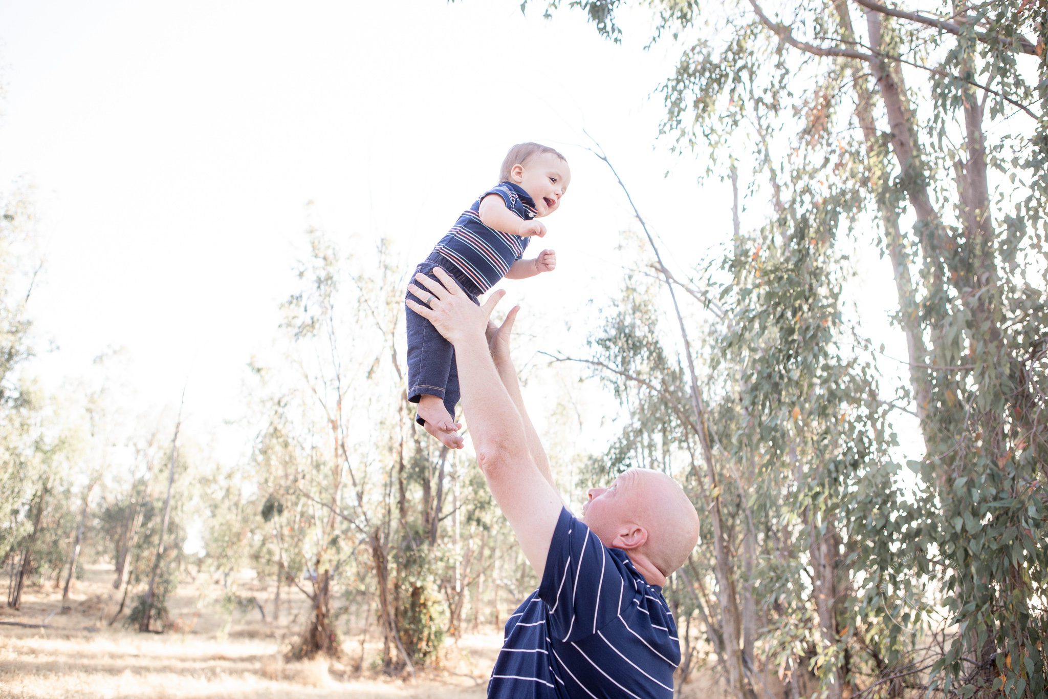 Family pictures in a field, dad throwing baby in the air smiling, One Good Shot Photography
