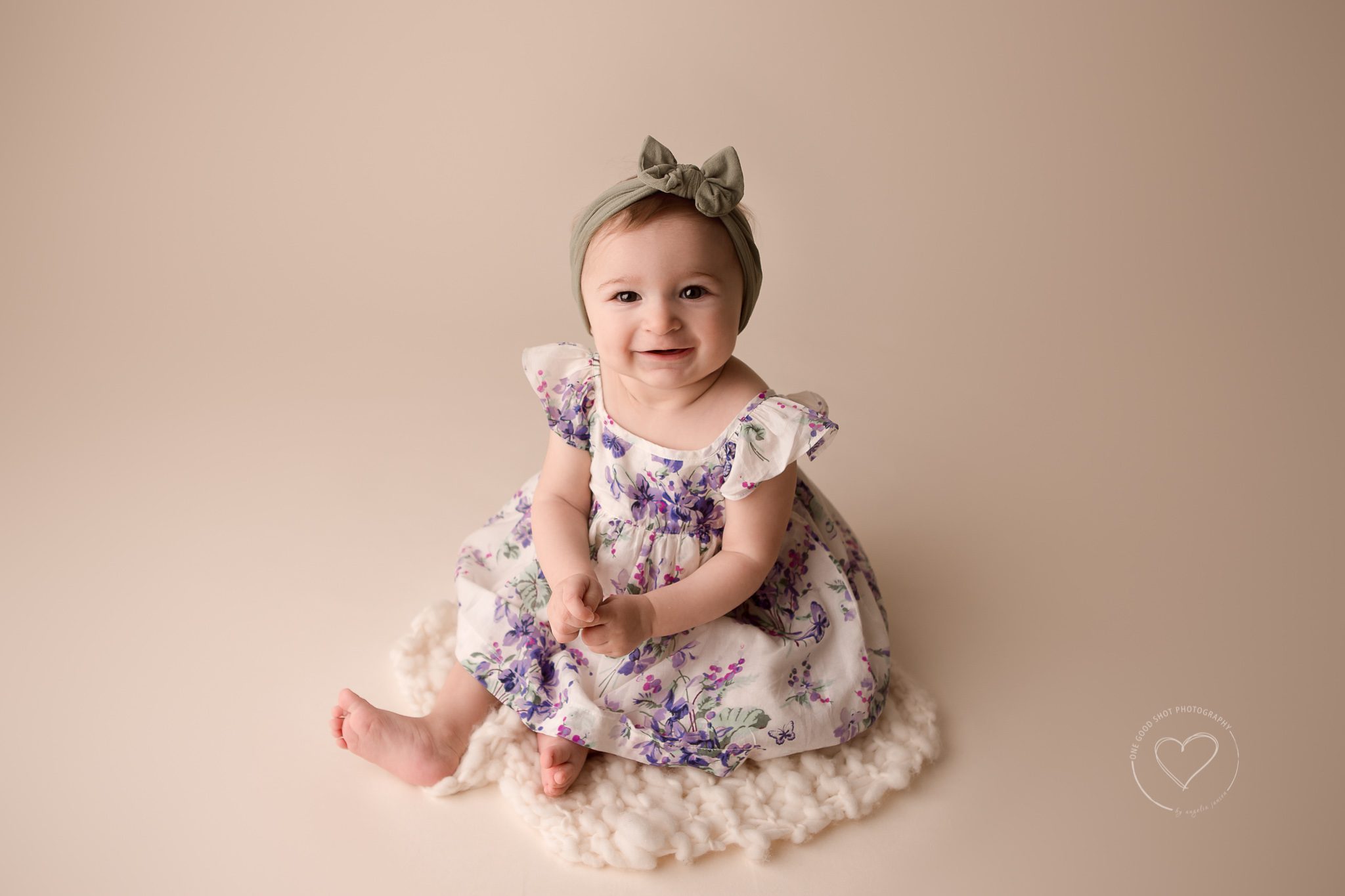 6 Month old baby girl wearing lavender floral dress, sitting, smiling