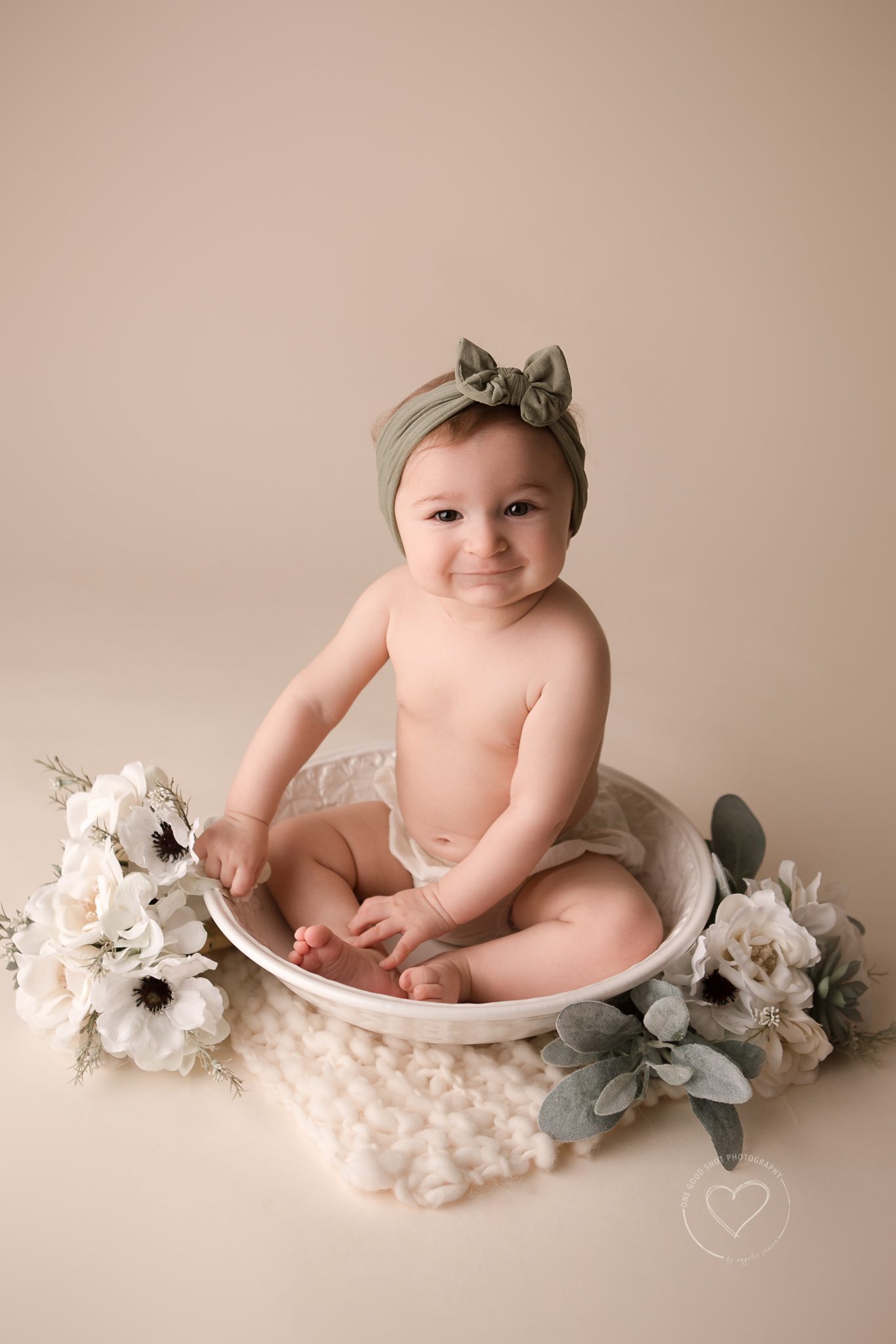 6 Month old, Baby Girl, Milestone session, sitting in a bowl surrounded with white flowers, smiling at camera, wearing green bow