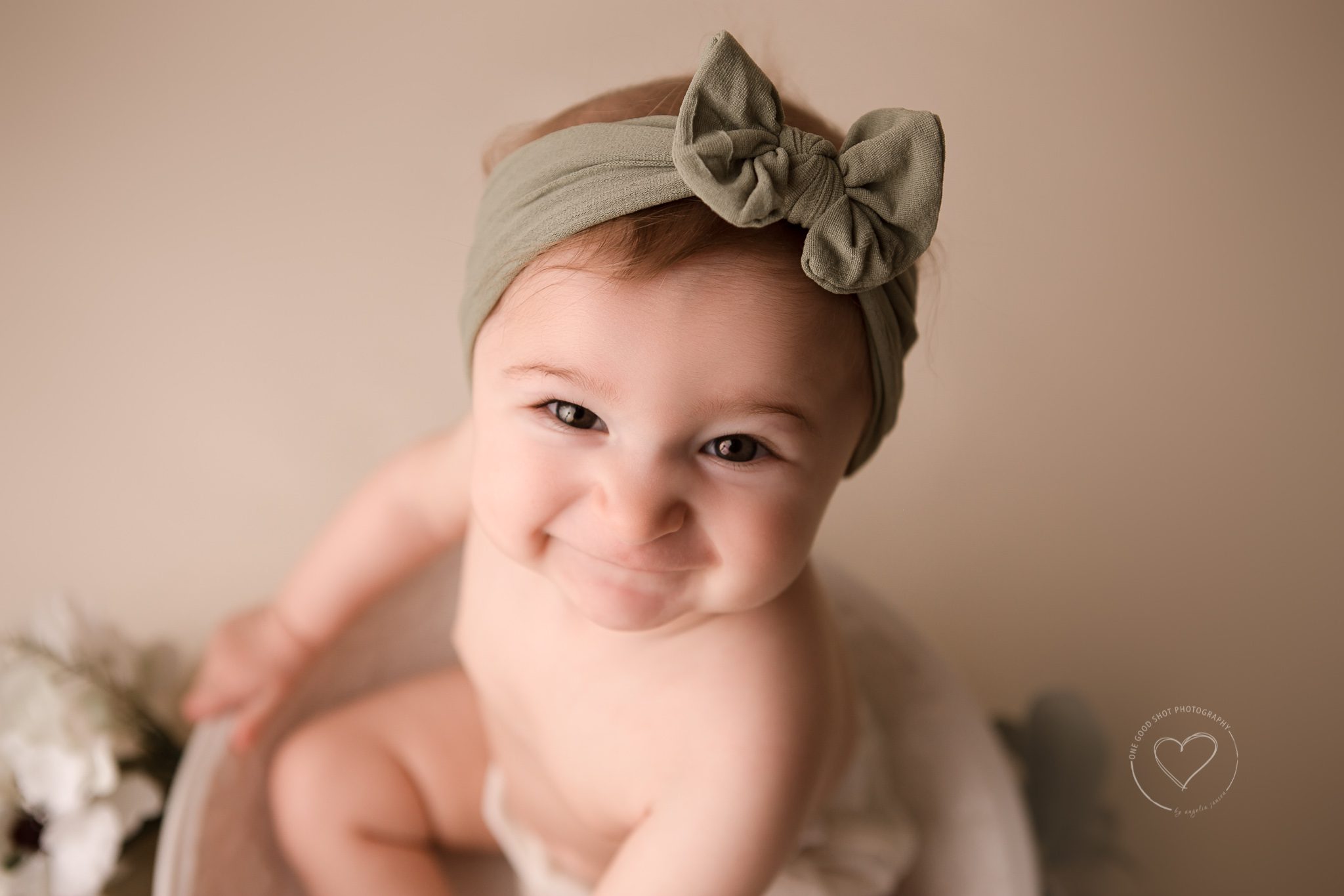 Baby girl, Sitting, 6 months old, smiling at camera, wearing green bow