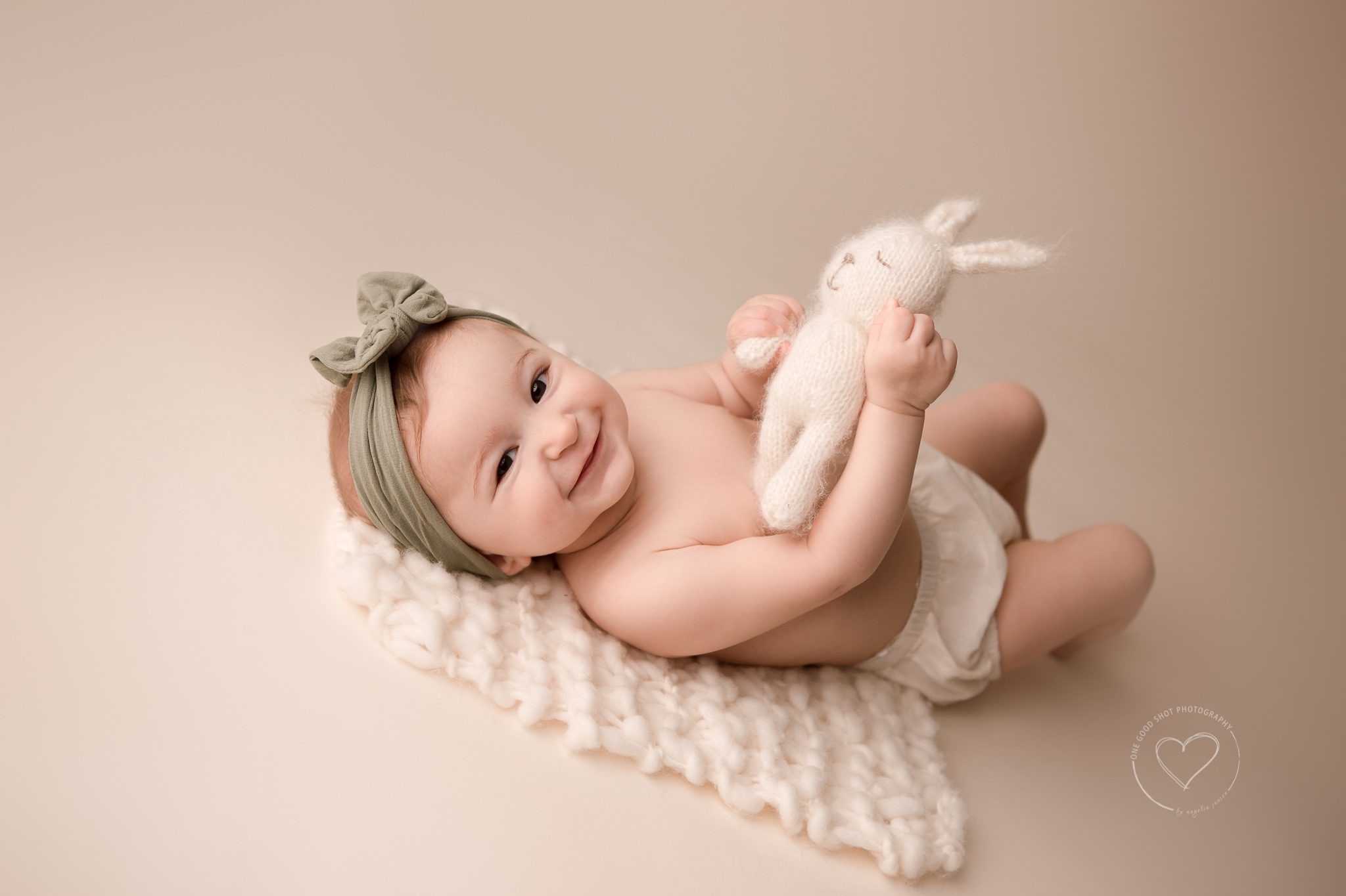 Baby photography, Baby girl lying on back holding bunny smiling, wearing green bow