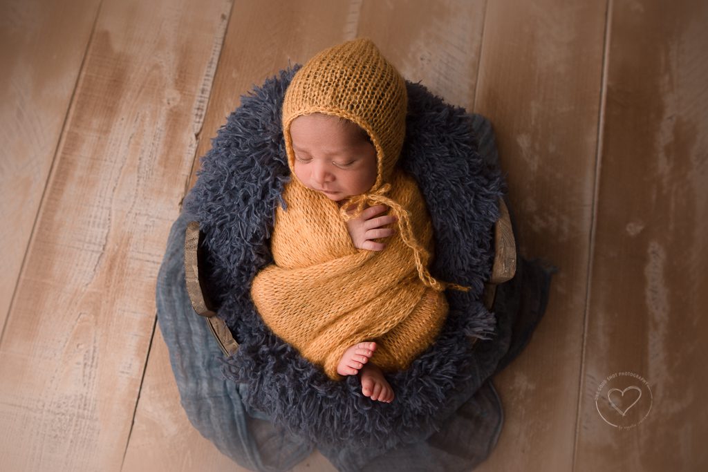 newborn photos, baby wrapped in yellow with bonnet laying on blu fur in a bucket, fresno newborn phoographer