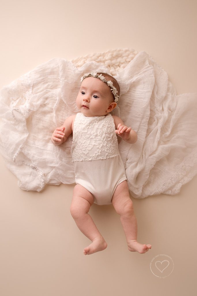 3 month old baby girl milestone photos, white romper, floral halo, happy baby lying on white layer, fresno, photographer