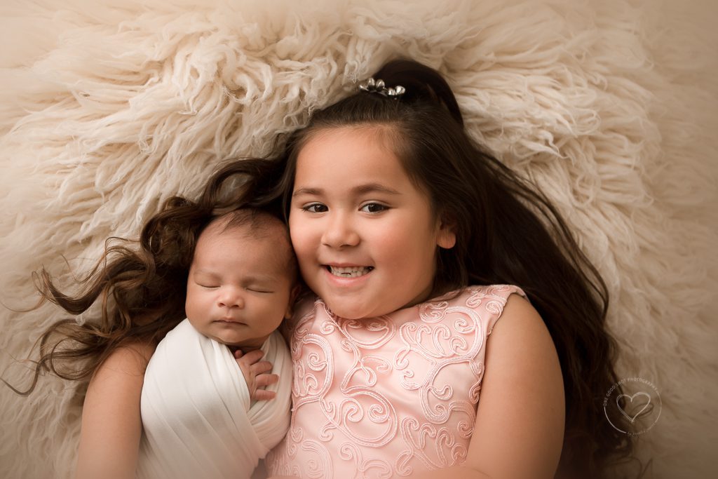 newborn photography, cousins, big girl holding baby on flokati