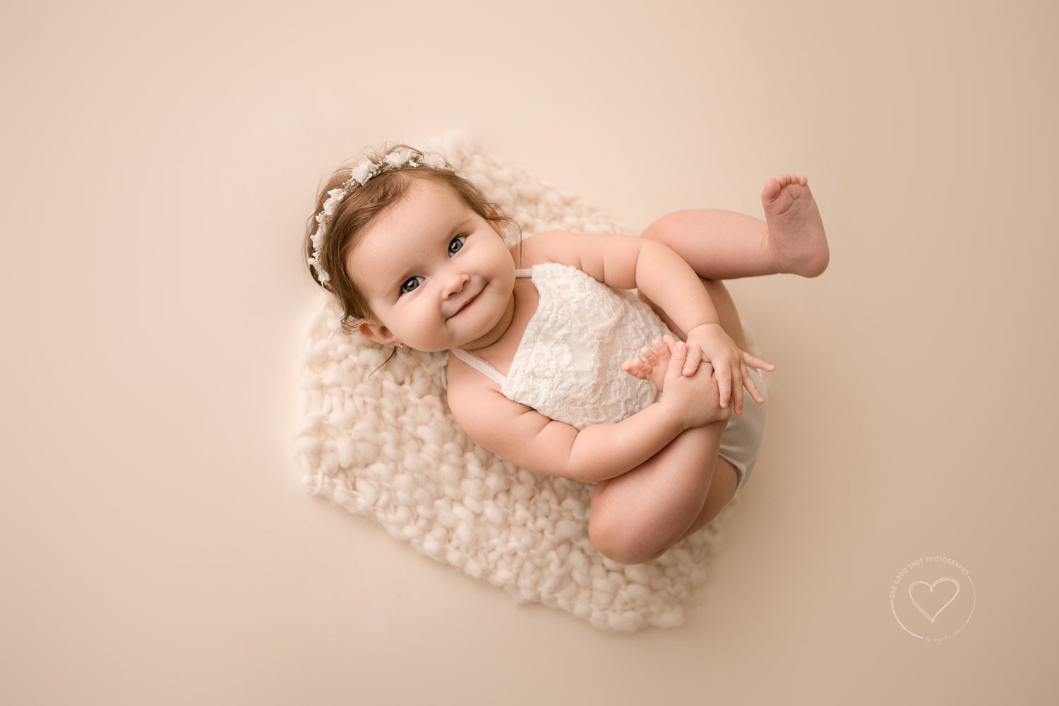 baby girl milestone photos, 6 months old, laying down, looking up at camera grabbing feet, white romper, floral halo, fresno, clovis, photographer 