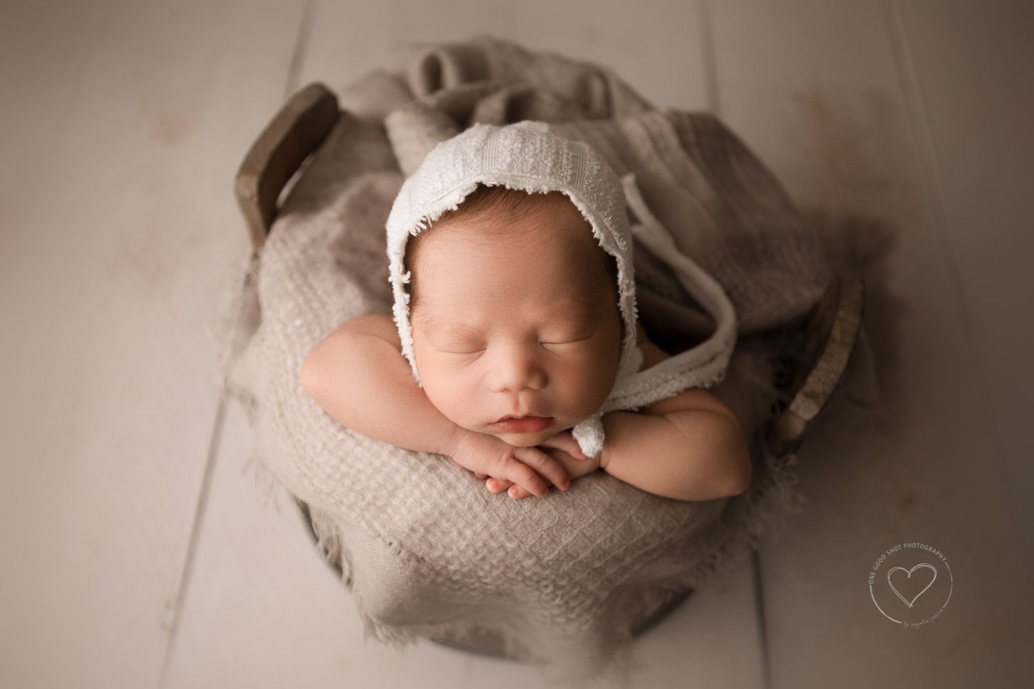 Newborn baby boy, Bucket pose, head on hands, wearing white bonnet, neutral colors, fresno photographer