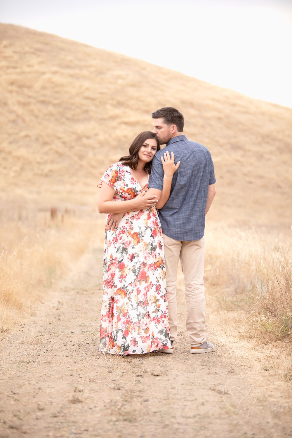 maternity, mom and dad close together, dad kissing mom's head, floral dress, dry grassy foothills, fresno, clovis, photographer