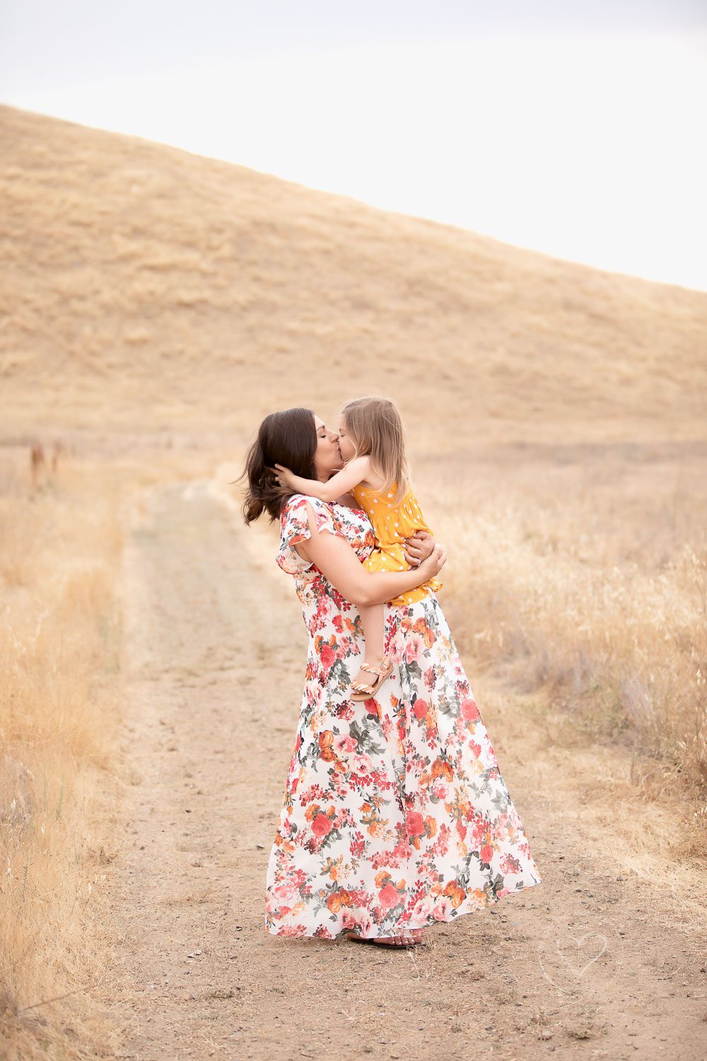 maternity, mom wearing floral dress holding big sister and kissing, grassy foothills, fresno, clovis, photographer