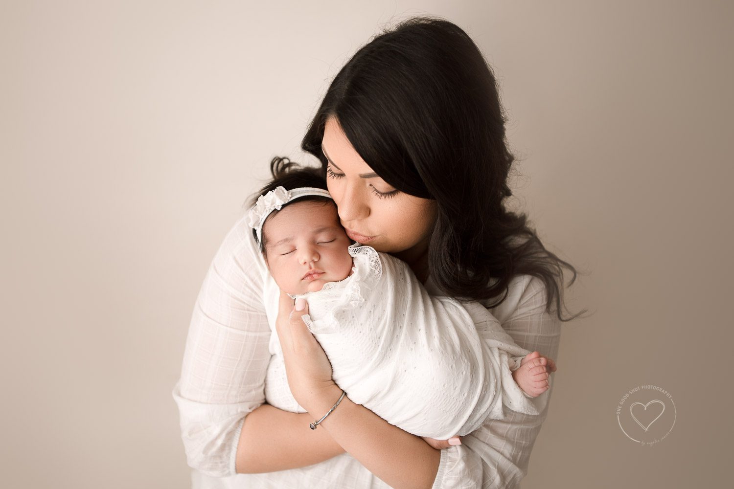 Mom kissing baby, wrapped in whote, floral headband, neutralsm fa ily, love, Fresno newborn photographer